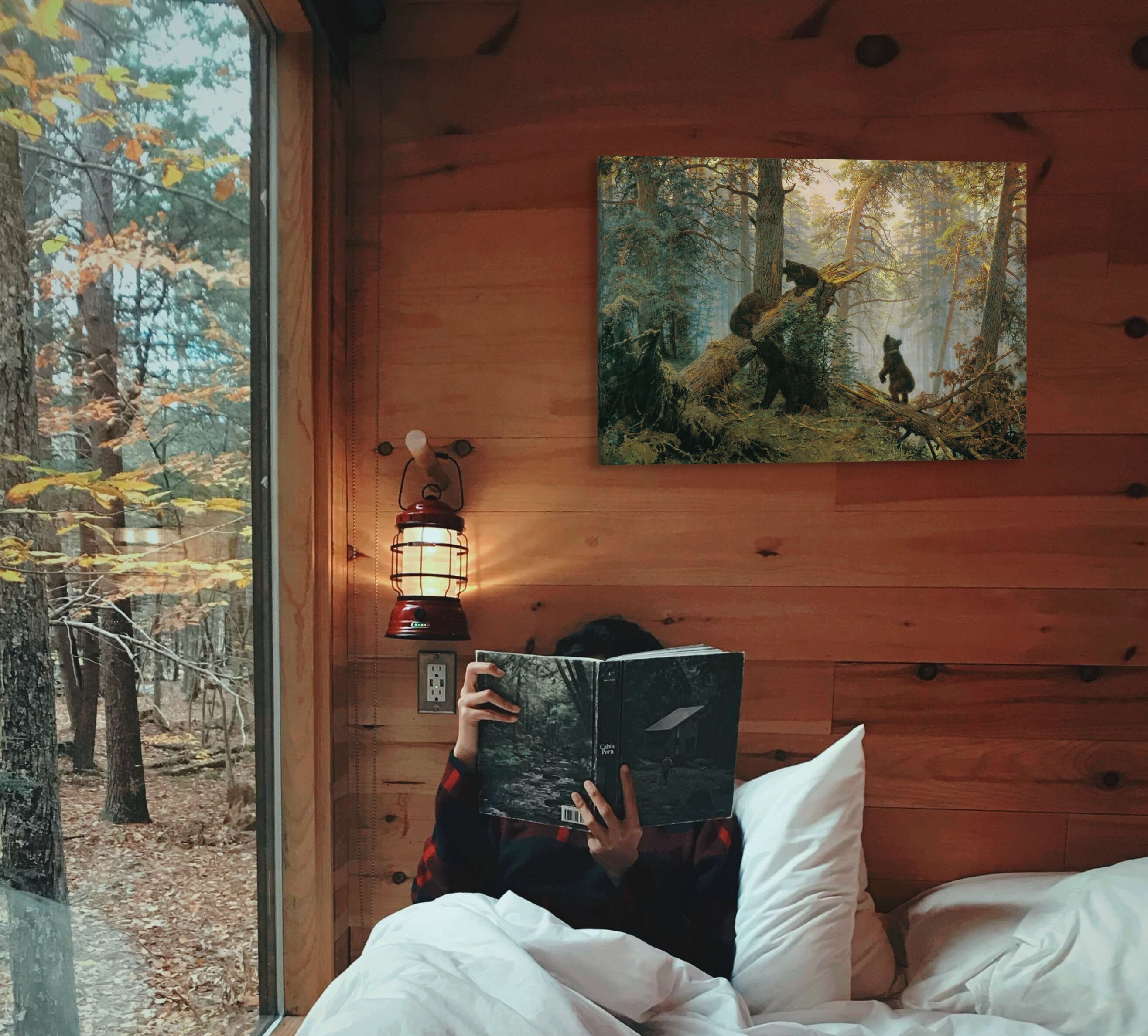 A large, horizontal 20x30" inch easy to hang canvas print featuring a vintage oil painting by Ivan Shishkin hung above a bed in a cabin bedroom overlooking a forest.