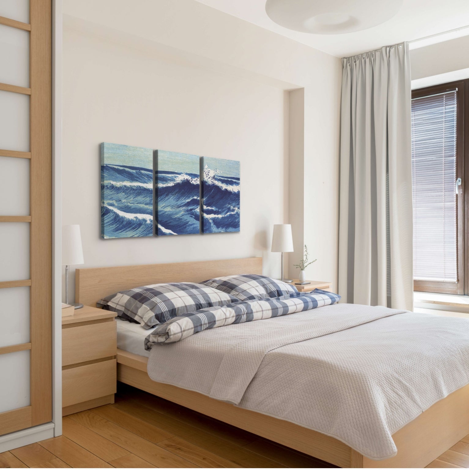 A set of three, vertical easy to hang canvas prints all sharing the same image of a painted wave across the panels, hung above a bed in a coastal themed bedroom. 