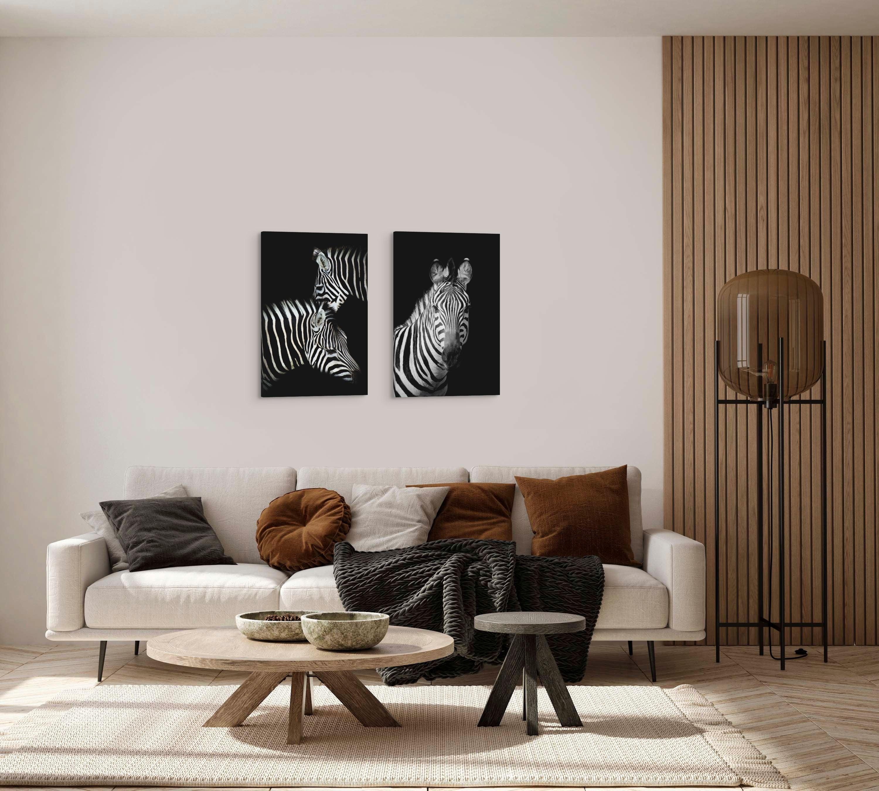 A set of two, vertical 20x30" inch easy to hang canvas prints featuring black and white photographs of zebras, hung above a couch in a living room. 