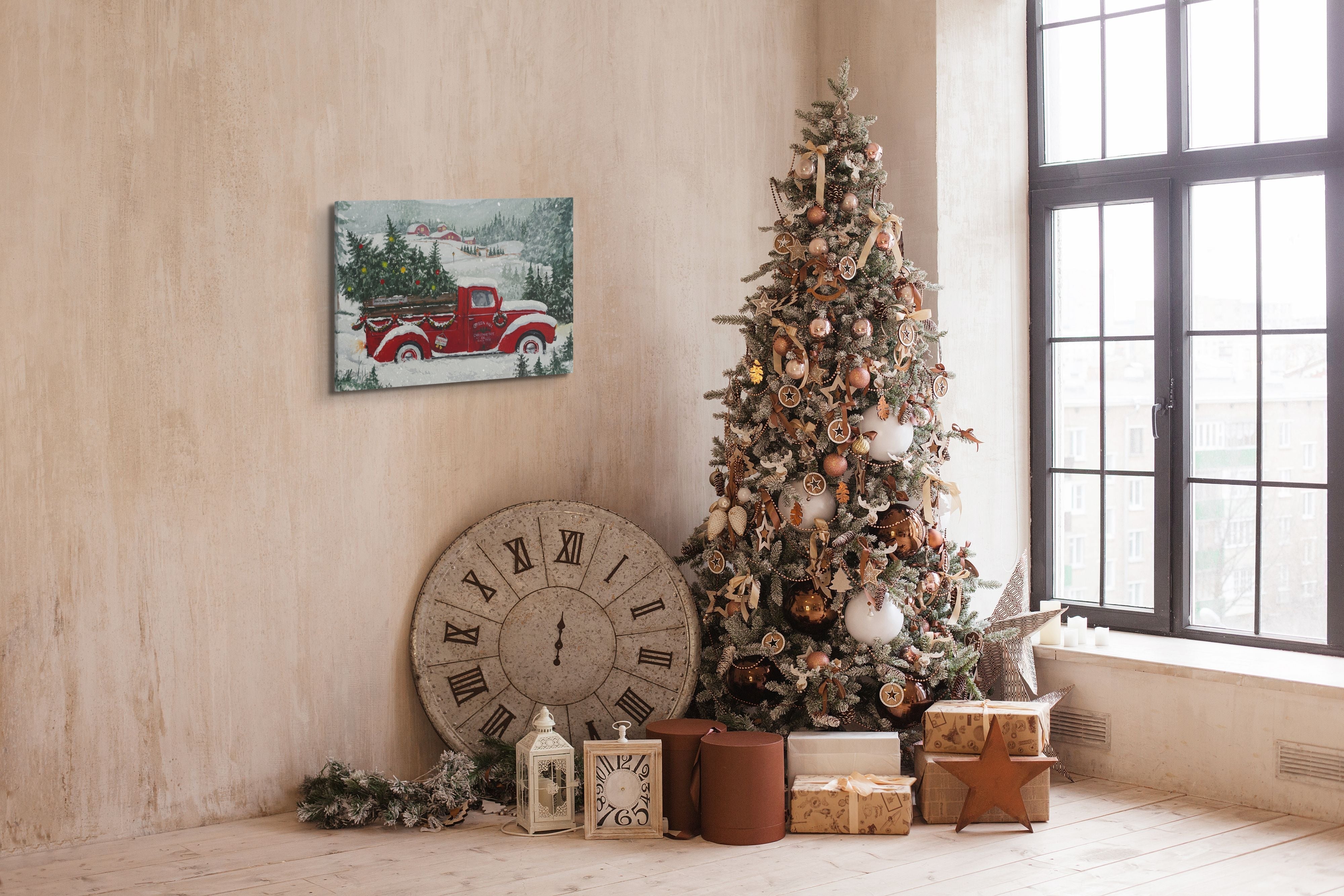 An easy to hang, horizontal 20x30" inch canvas print, featuring a red truck with a christmas tree in the trunk, hung beside a real, decorated Christmas tree in a living room. 