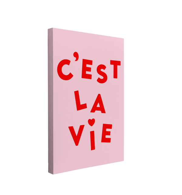 Single, 2:3 vertical easy to hang canvas print on a transparent background featuring an image of fun red font, "C'est la Vie" with a heart on the i in vie, on a light pink background.