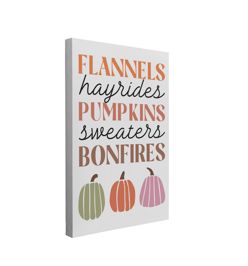 Single, 2:3 vertical easy to hang canvas print on a transparent background featuring an image of the words "Flannels, hayrides, pumpkins, sweaters, bonfires" in different shades of orange pink and brown with three pumpkins under the words on a light grey background.