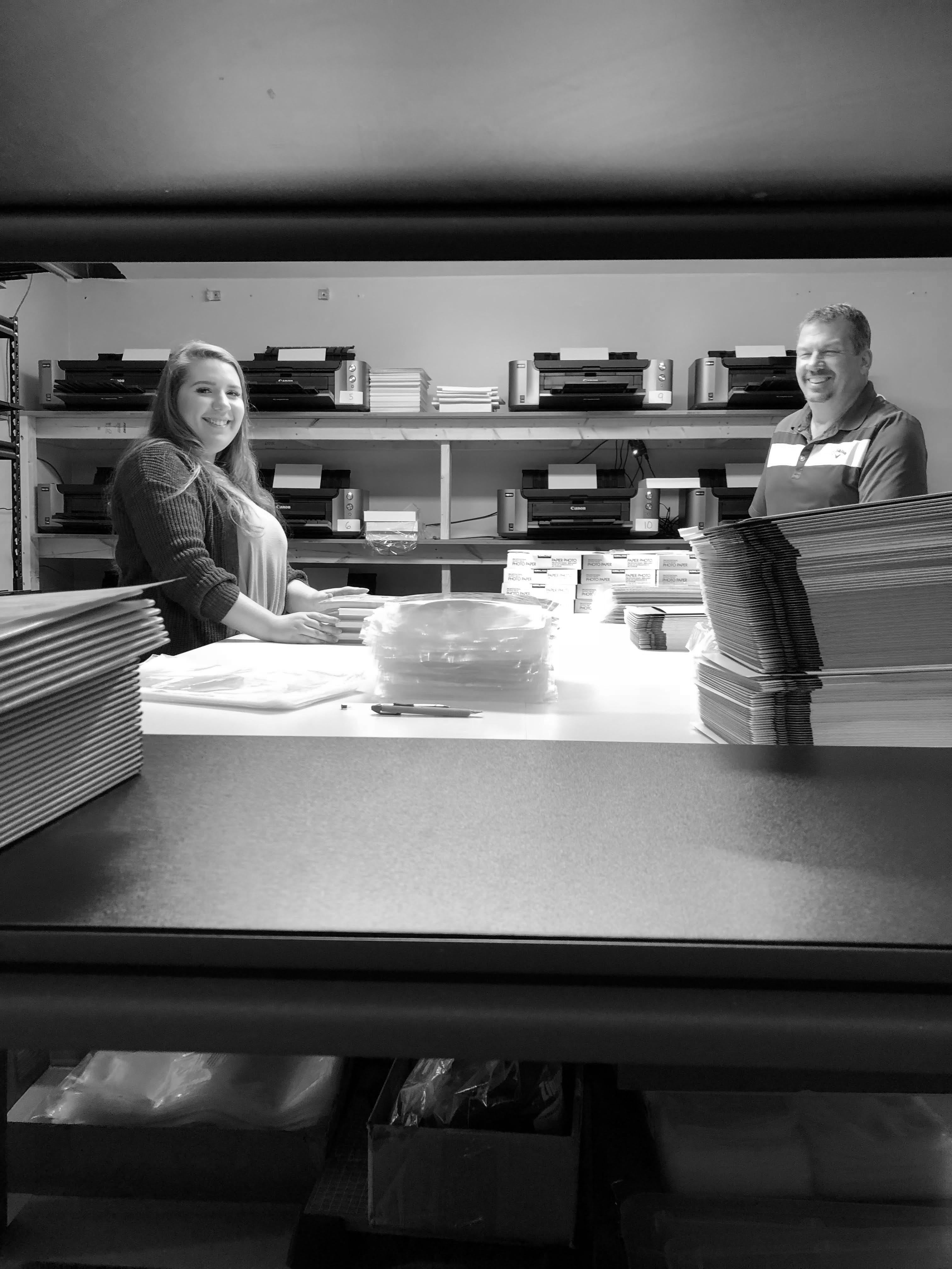 Sara and Ron packing prints at a table surrounded by printers. 