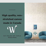 Lifestyle image of the vertical, 12x18” inch easy to hang canvas wall art hung in a coastal blue living room in-between two chairs with graphic saying "High quality, non-stretched canvas made in Canada"