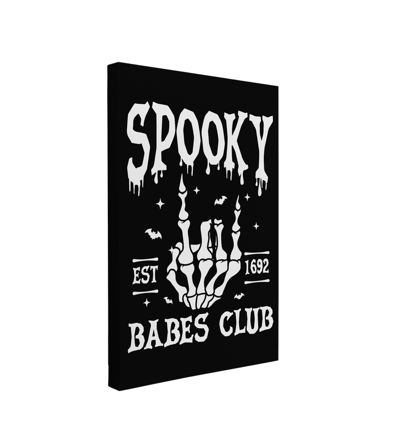 Single, 2:3 vertical easy to hang canvas print on a transparent background featuring an image of black and white skeleton hand doing the "Rock on" hand jesture with white words, "Spooky Babes Club, est 1692" on a black background