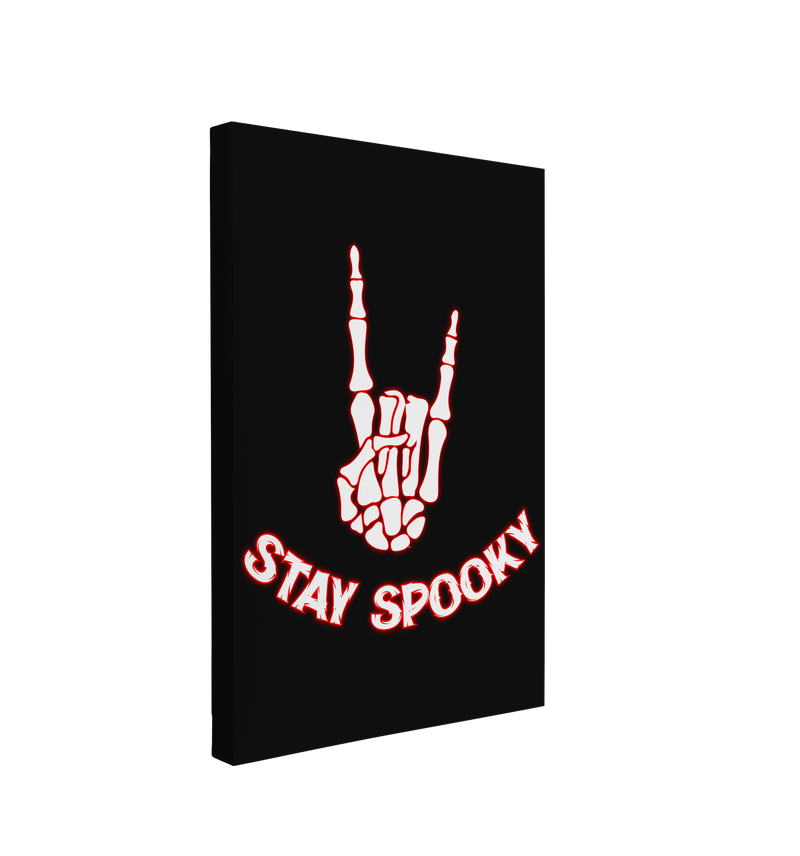 Single, 2:3 vertical easy to hang canvas print on a transparent background featuring an image of a white skeleton hand making the "Rock on" gesture, with a red outline on a black background with words "Stay Spooky" under it in a similar format. 